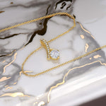 Allure necklace in 18k gold finish draped gracefully across a marble slab.