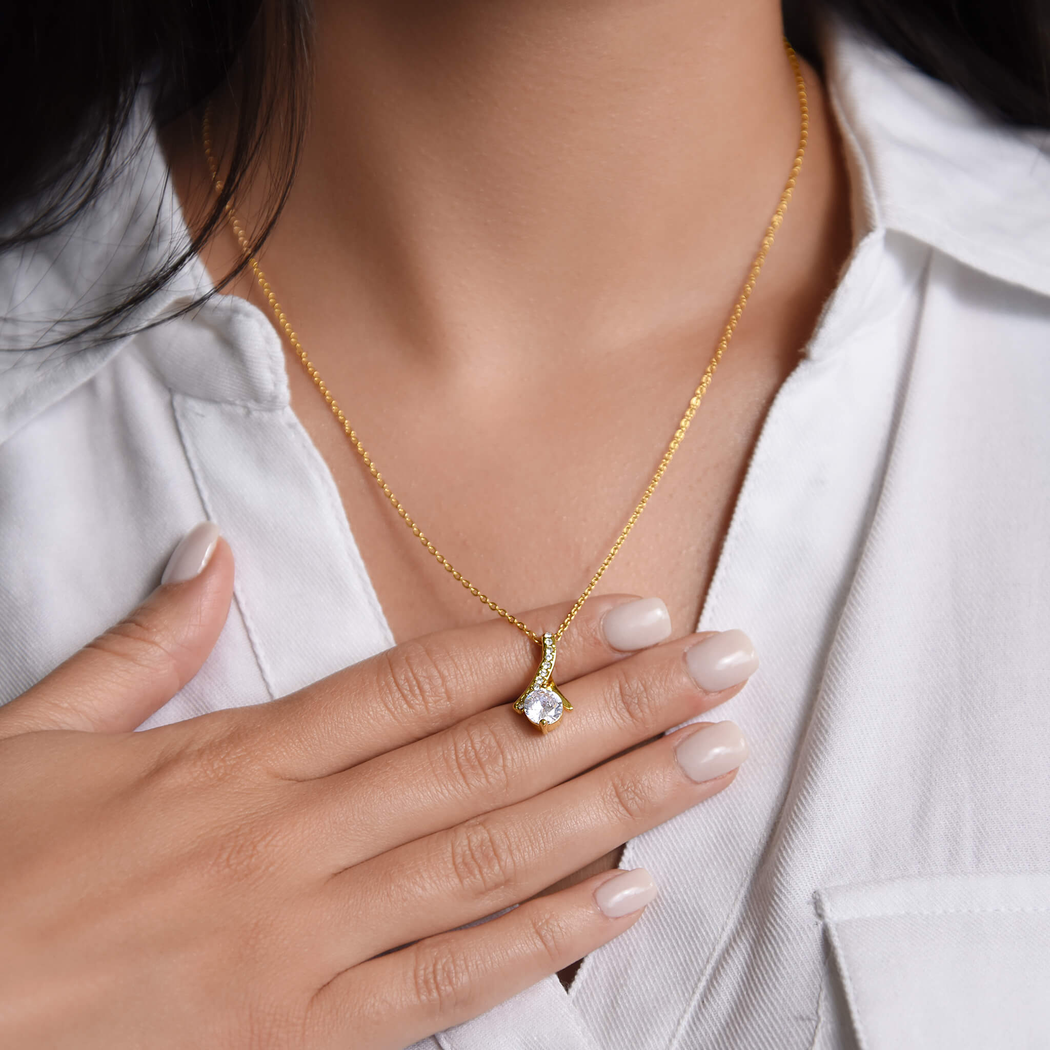 Model wearing the Allure necklace in 18k gold finish with a white collared blouse. Her hand rests gently on her chest behind the necklace, highlighting the pendant's dainty size.