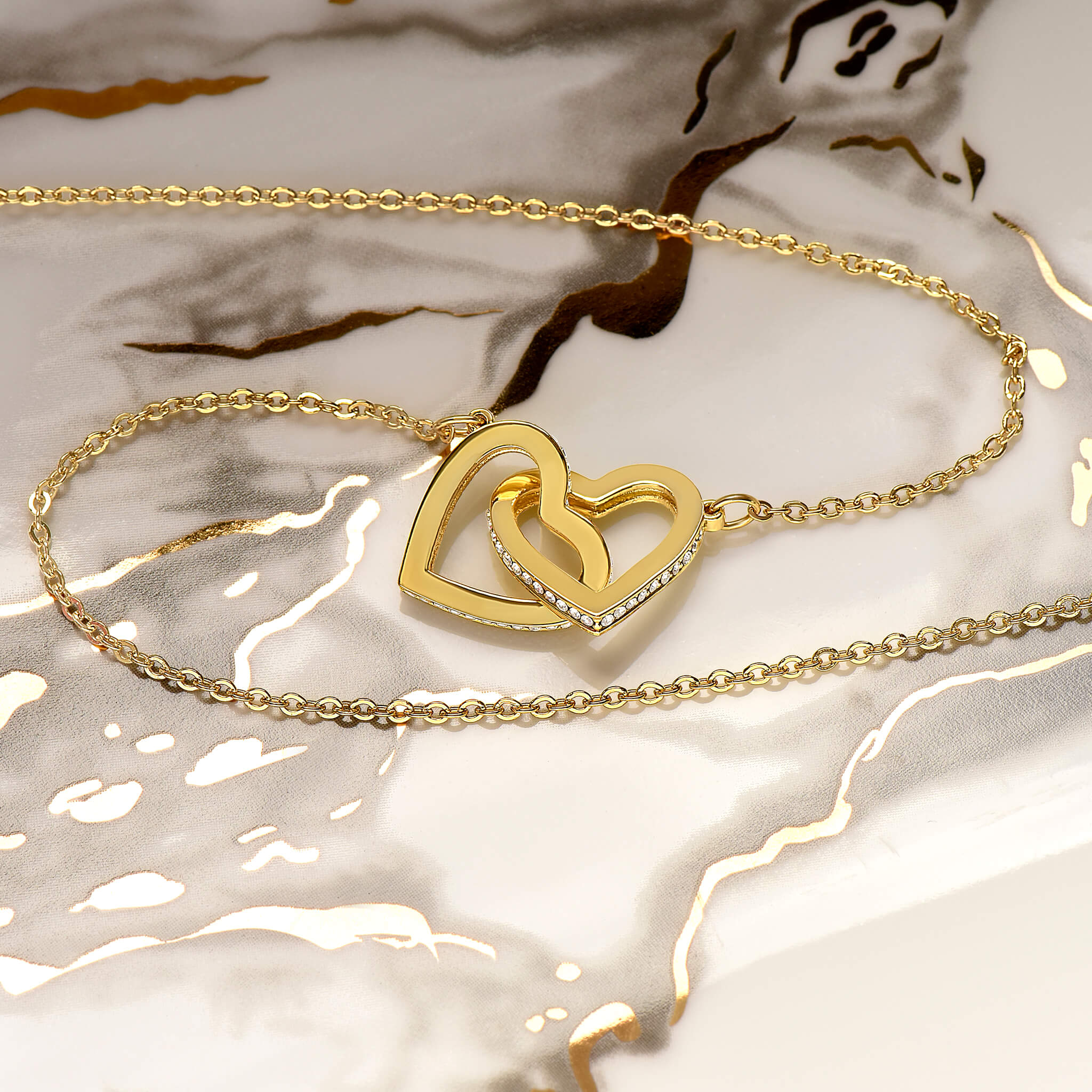 Gold interlocking hearts necklace draped gracefully over a marble background