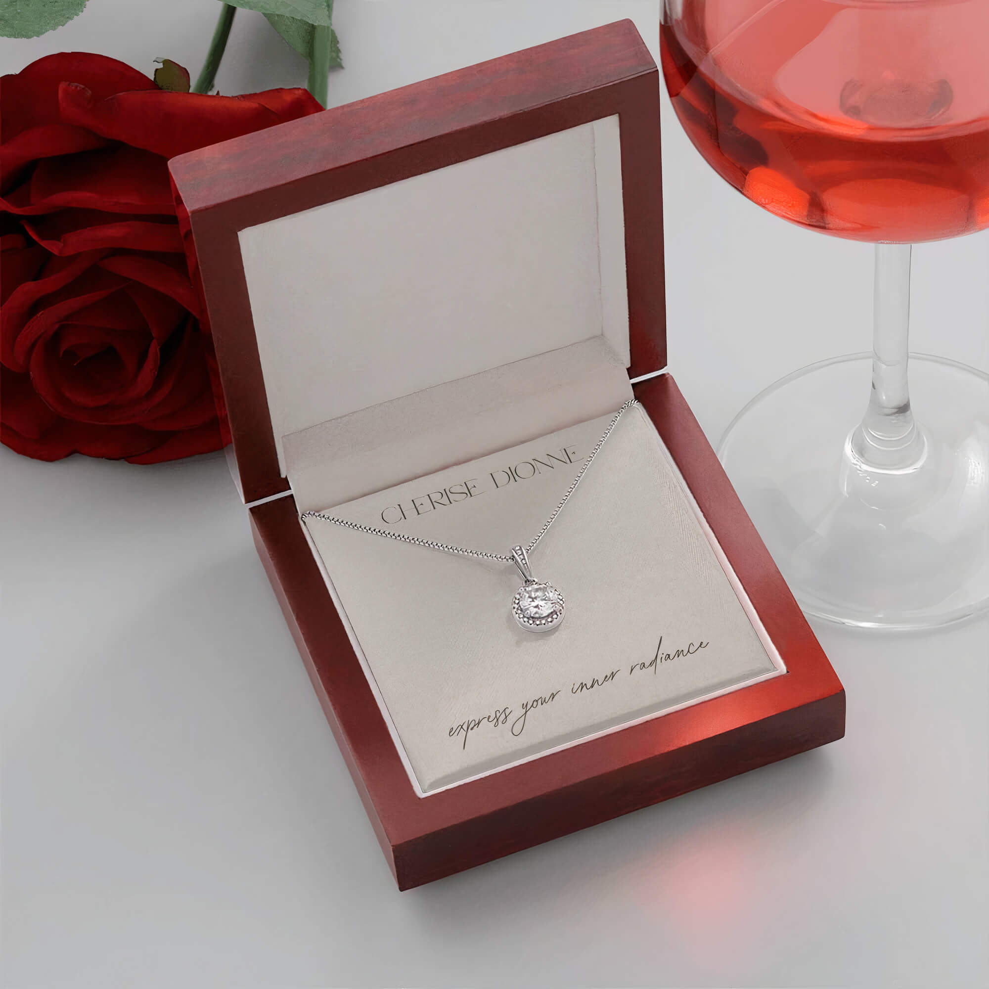 Prosperity necklace packaged in an elegant gift box with a card that features the Cherise Dionne logo and the phrase 'express your inner radiance', with a red rose and a glass of wine in the background.